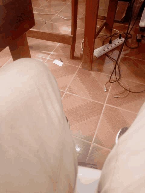 a person 's feet on a tiled floor next to a wooden table and a power strip