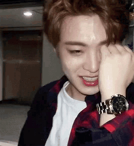 a young man wearing a watch is covering his face with his hand .