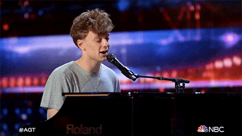 a young man sings into a roland microphone while playing a piano