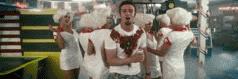 a group of people are standing around a man in a white shirt with blood on his shirt .