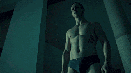 a shirtless man with a tattoo on his chest holds a gun