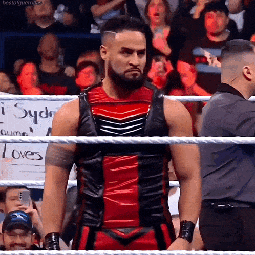 a man in a red and black outfit is standing in a wrestling ring in front of a crowd