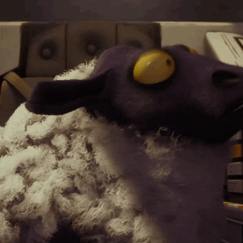 a stuffed purple sheep with yellow eyes is sitting on a counter