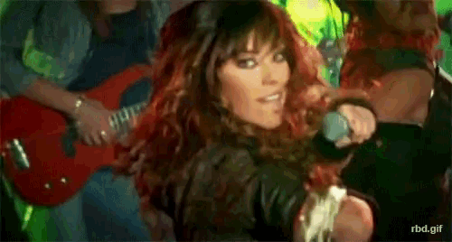 a woman with red hair is singing into a microphone while a man plays guitar in the background