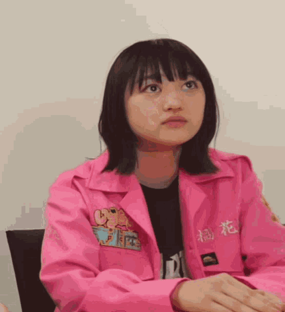 a young girl wearing a pink jacket with chinese writing on it is sitting at a table .