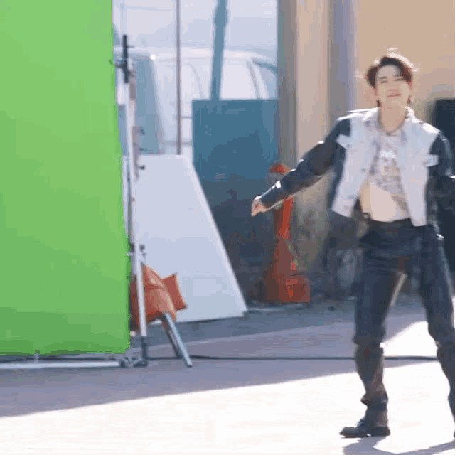 a man is dancing in front of a green screen in a parking lot .