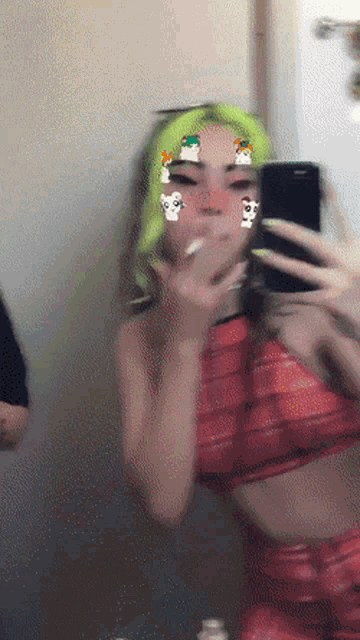 a woman with green hair is taking a picture of herself in a mirror