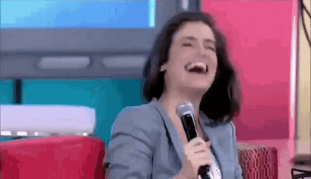 a woman is laughing while holding a microphone in front of a television .