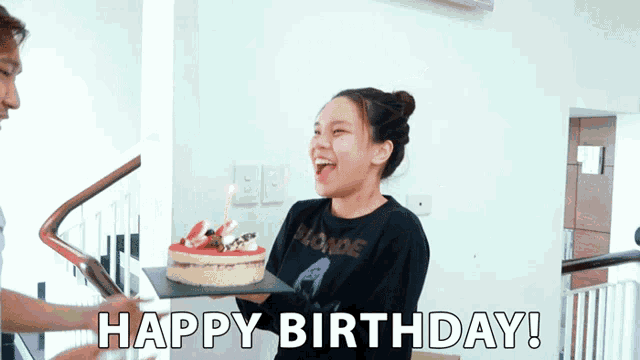 a woman in a blonde shirt is holding a birthday cake and says happy birthday