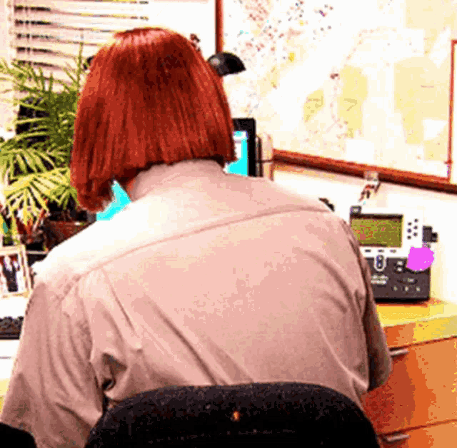 a woman with red hair sits at a desk with a telephone and a map on the wall