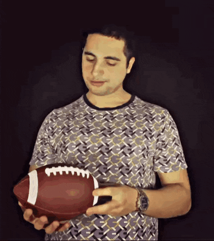 a man is holding a football with the letter t on it
