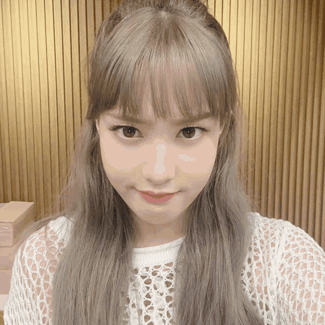 a woman with gray hair and a white top looks at the camera