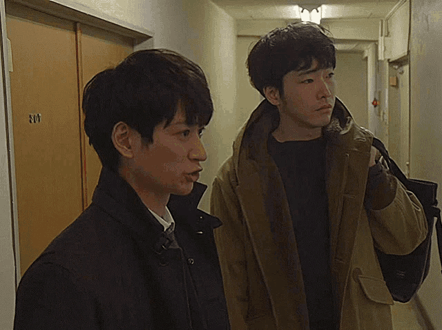 two men are standing next to each other in a hallway with a door that has the number 301 on it