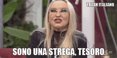 a woman with blonde hair and glasses is sitting on a couch and talking in a language other than english .