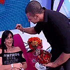 a man is serving a woman a bouquet of flowers while she sits on a couch .