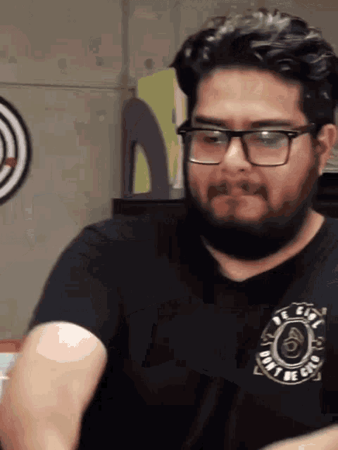 a man with glasses and a beard wears a black shirt that says " dont be a clone "