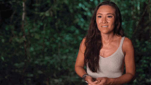 a woman in a white tank top is standing in the woods