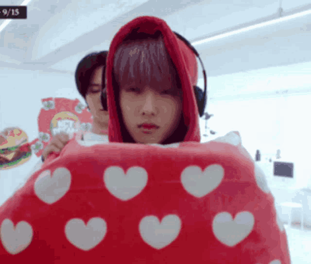 a man in a red hoodie is holding a red heart shaped pillow