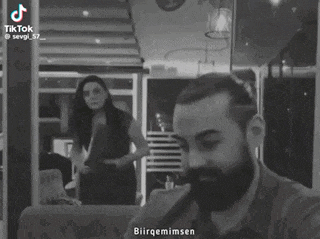 a man with a beard is sitting in front of a woman who is standing behind him