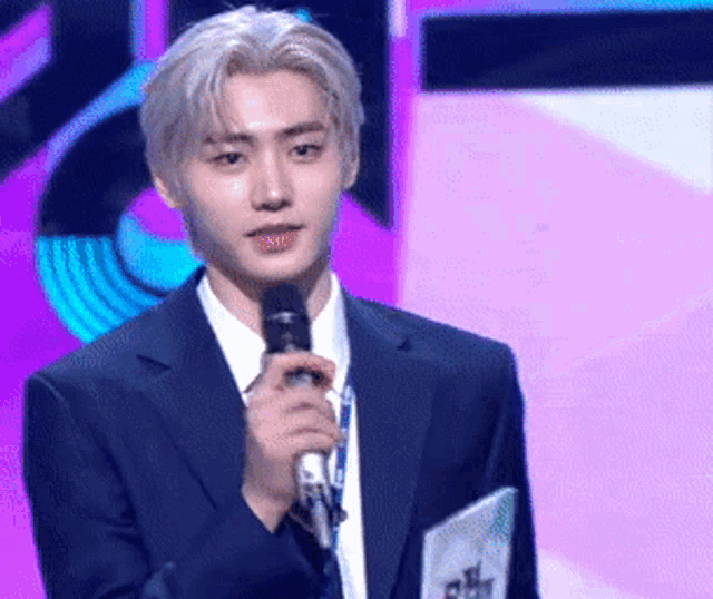a man in a suit is holding a microphone in front of a purple background .