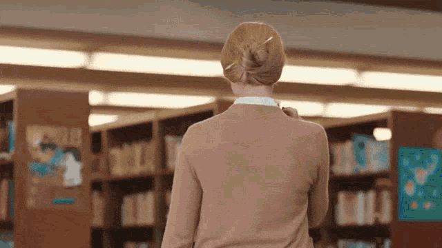 a woman is walking through a library looking at books