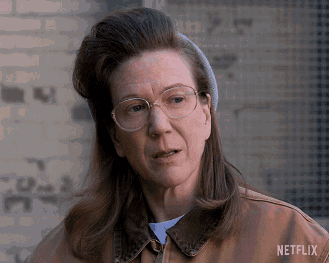 a woman wearing glasses and a brown jacket with netflix written on it