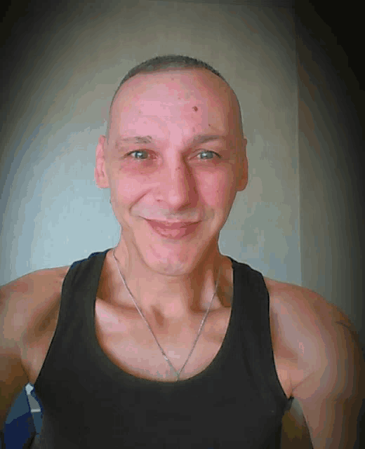 a smiling man wearing a black tank top and a silver necklace