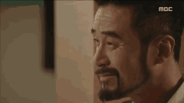 a man with a beard is crying while sitting in front of a wall .