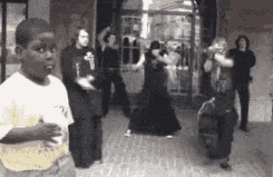 a boy is standing in front of a group of people dancing on the street .