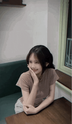 a young woman sits at a table with her hand on her face
