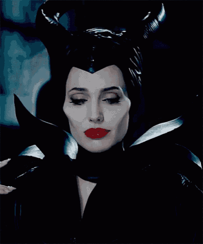 a woman in a black costume with horns and red lips smiles