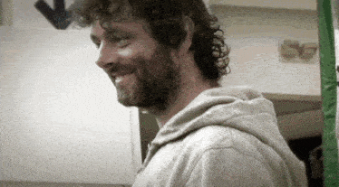 a man with curly hair and a beard smiles in front of a sign that says 50