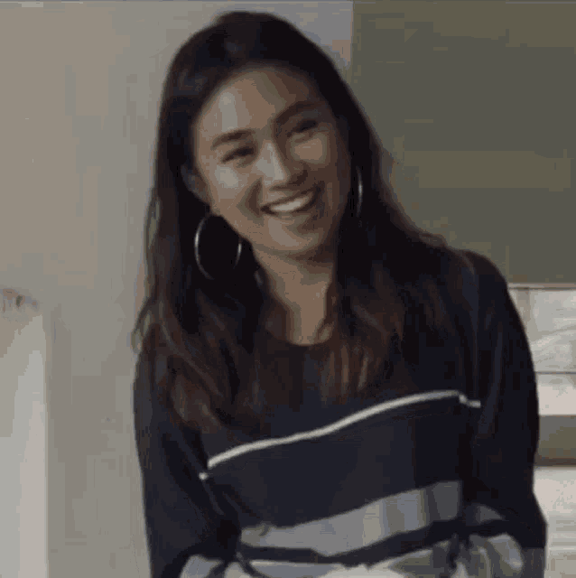 a woman is smiling and wearing hoop earrings and a striped shirt .