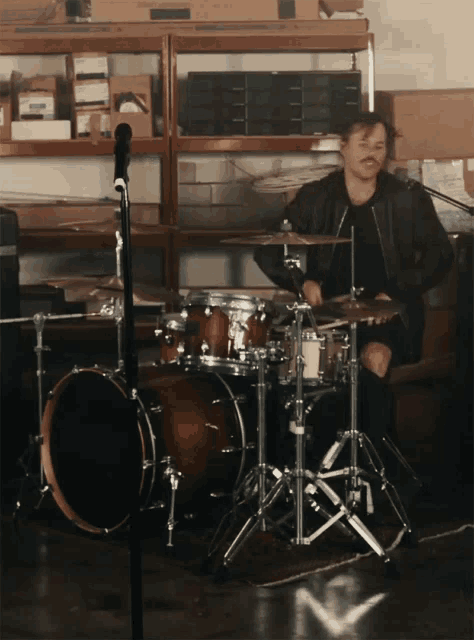 a man playing drums in a room with boxes on shelves behind him