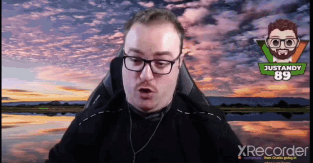 a man wearing glasses and a justandy 89 logo behind him