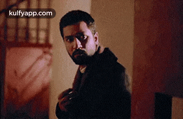 a man with a beard is standing in a dark room with a gun in his hand .
