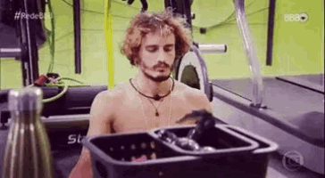 a shirtless man is sitting on a treadmill in a gym next to a laundry basket .