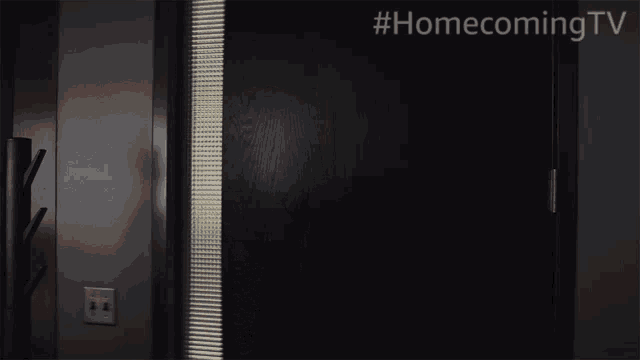 a woman is standing in a dark room with #homecomingtv written on the bottom