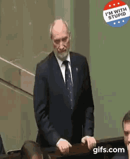 a man in a suit and tie is standing in front of a sign that says `` i 'm with stupid ''