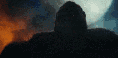 a giant gorilla is standing in front of a full moon in the dark .