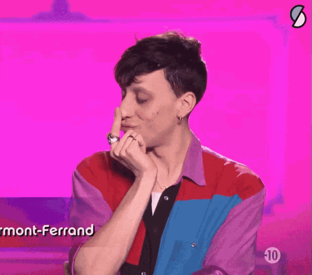 a man in a colorful shirt holds his finger to his nose in front of a sign that says mont-ferrand