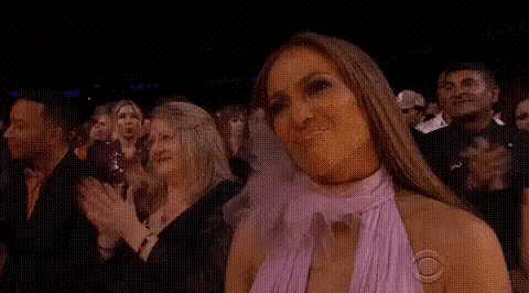 a woman in a purple dress is sitting in a crowd of people clapping .