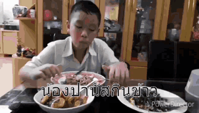 a young boy is sitting at a table eating food with a fork and spoon .
