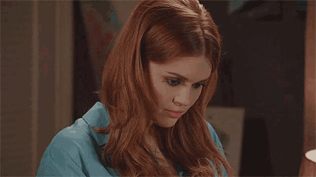 a woman with red hair and a blue shirt is looking at the camera