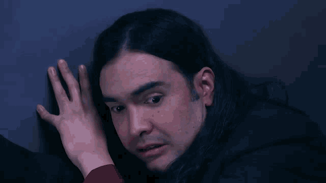 a man with long hair is smiling while putting his hand on a wall .