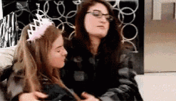 two young women are sitting next to each other on a couch . one of the girls is wearing a pink tiara .