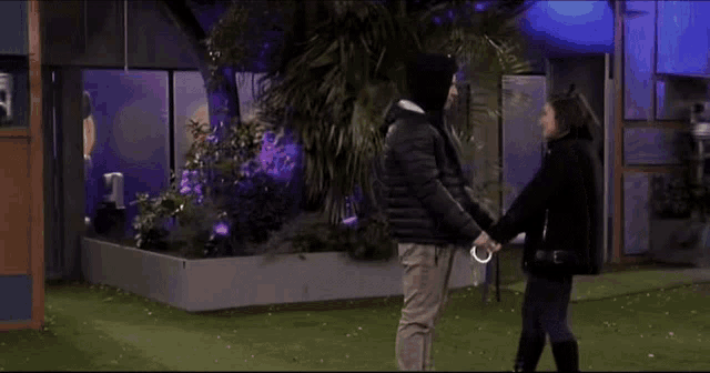 a man and a woman are holding hands in front of a building with purple lights