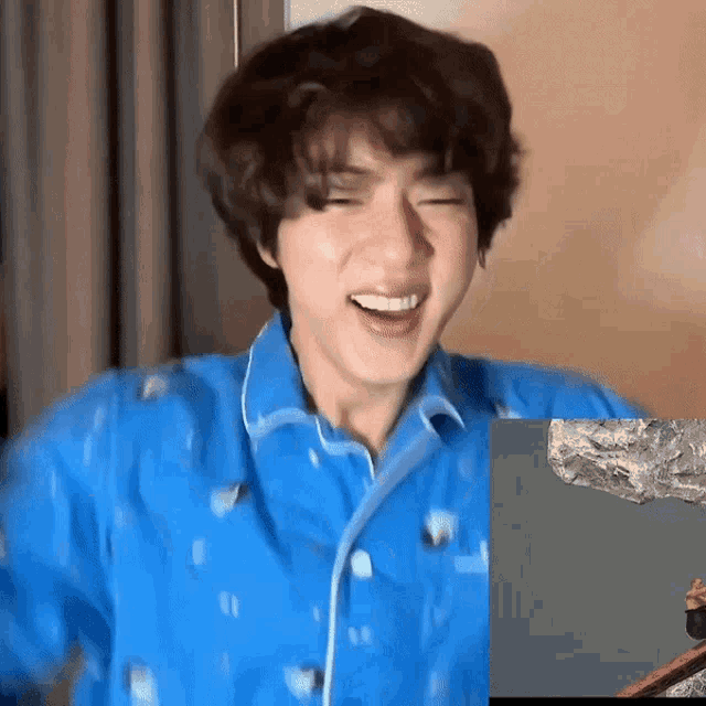 a young man wearing a blue shirt is laughing while looking at a picture of a mountain .