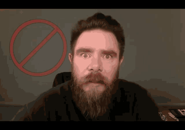 a man with a beard stands in front of a red circle with an x in it