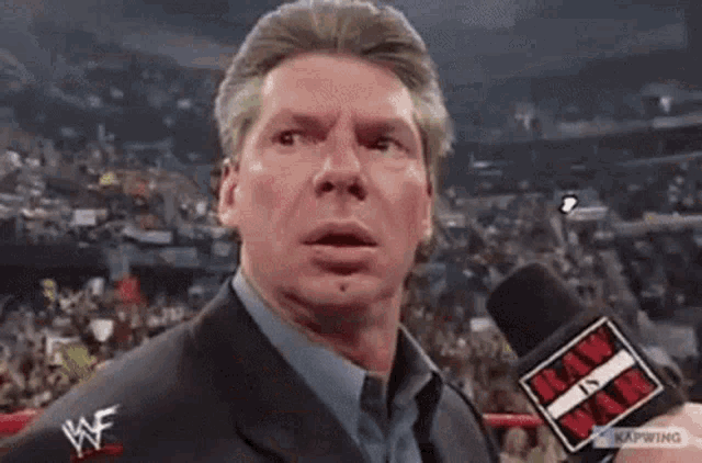 a man in a suit and tie is holding a microphone in a wrestling ring .